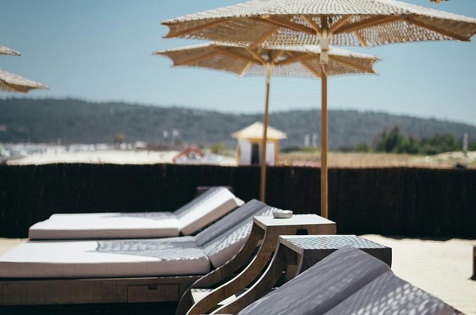 Wooden beach loungers under straw parasols on pale sand