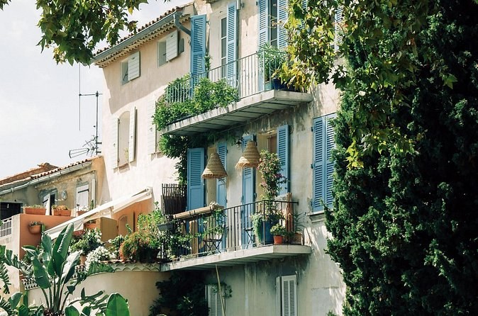 A pastel house with green shutters and balconies behind a tangle of garden plants