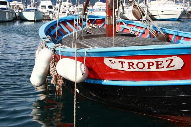 A red and blue wooden fishing boat, its bow painted St Tropez, moored among white boats