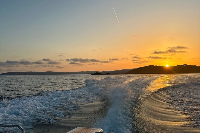 The sun going down over the gulf and its hills, seen over a boat's wake