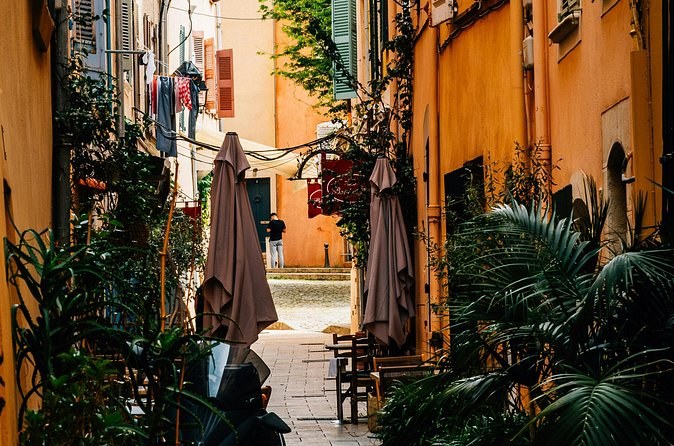 A narrow ochre lane with café umbrellas and potted palms